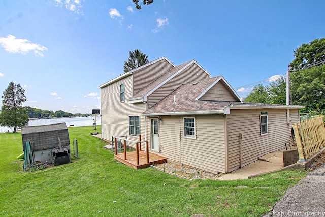 back of house featuring a deck with water view, a lawn, and roof with shingles