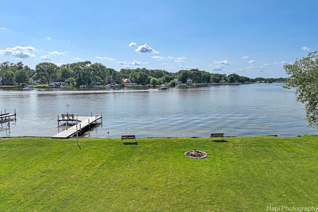 dock area featuring a water view, a fire pit, and a lawn