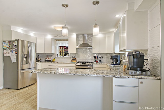 kitchen featuring stainless steel appliances, light wood-style flooring, a sink, a peninsula, and wall chimney exhaust hood