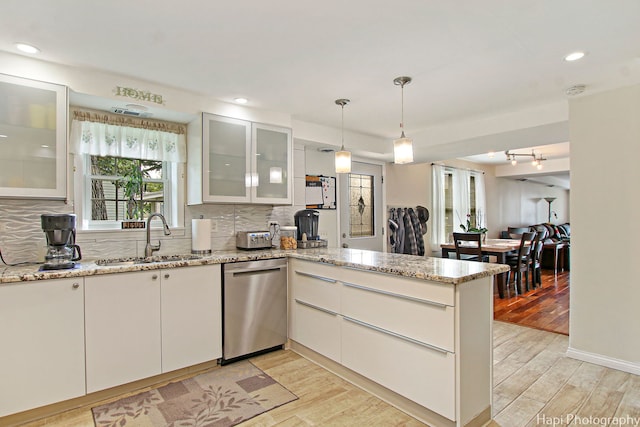 kitchen with light wood finished floors, decorative backsplash, a sink, dishwasher, and a peninsula