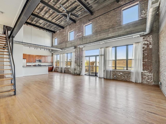 unfurnished living room featuring light wood-style floors, brick wall, a high ceiling, and stairway