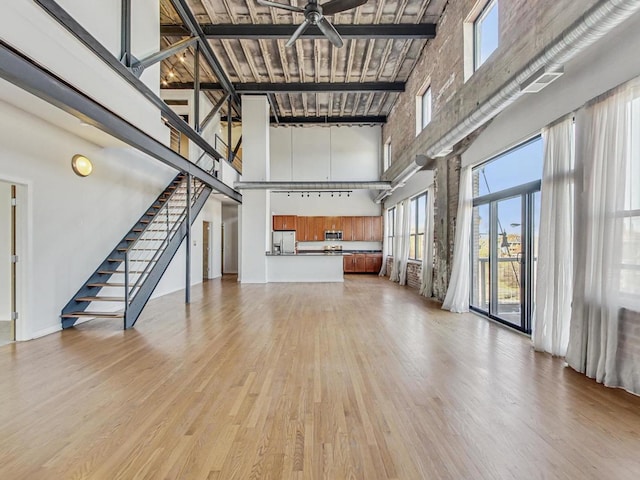 unfurnished living room featuring light wood finished floors, stairway, a high ceiling, and a ceiling fan