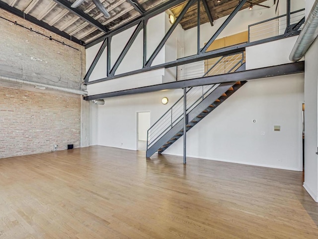 unfurnished living room featuring brick wall, wood finished floors, a towering ceiling, baseboards, and stairway