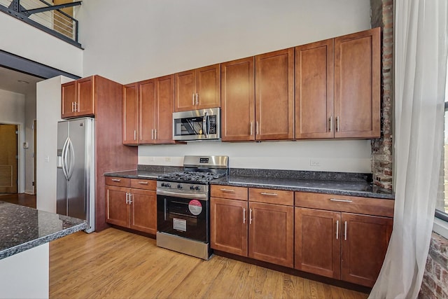 kitchen featuring dark stone counters, appliances with stainless steel finishes, a high ceiling, and light wood-style floors