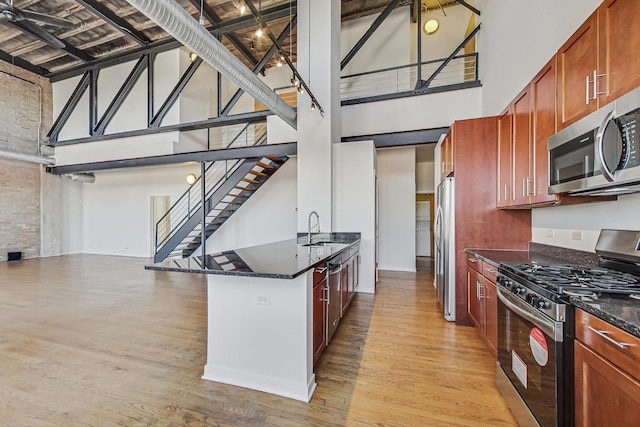 kitchen with a towering ceiling, light wood-style floors, stainless steel appliances, and a sink