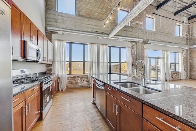 kitchen with light wood finished floors, stainless steel appliances, a high ceiling, a sink, and brick wall