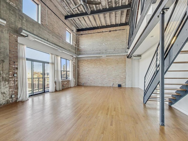 unfurnished living room with brick wall, a high ceiling, and wood finished floors