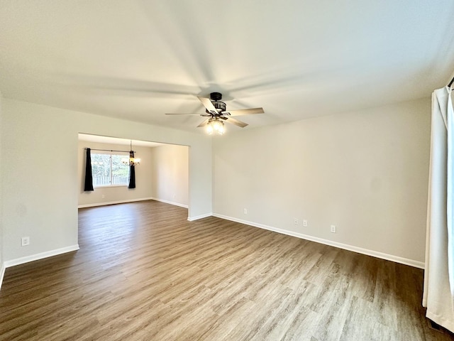 spare room featuring baseboards, dark wood-style flooring, and ceiling fan with notable chandelier