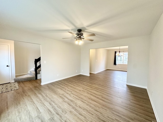 spare room featuring ceiling fan with notable chandelier, stairway, baseboards, and wood finished floors