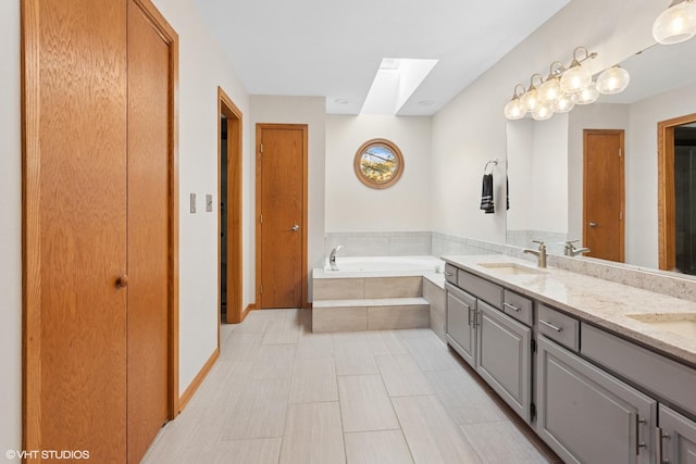 bathroom with baseboards, double vanity, a skylight, a bath, and a sink