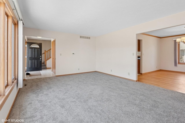 empty room featuring stairs, light colored carpet, visible vents, and baseboards