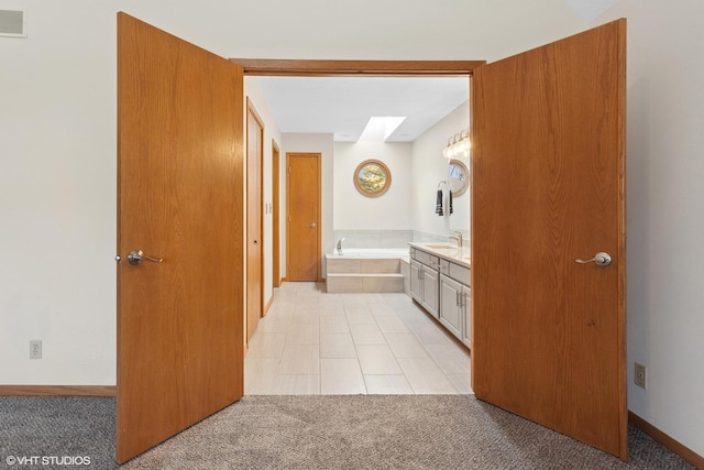 bathroom featuring vanity, a skylight, a bath, and baseboards