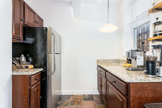 kitchen with stone tile floors, baseboards, freestanding refrigerator, light stone countertops, and open shelves