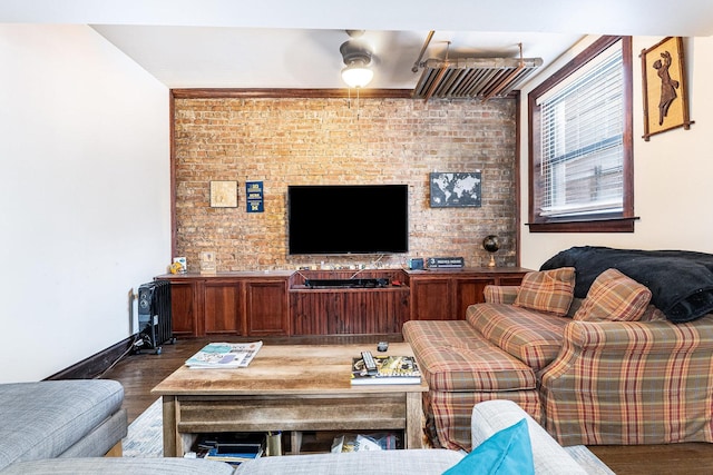 living area with brick wall, wood finished floors, a ceiling fan, and baseboards