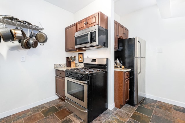 kitchen featuring baseboards, stainless steel appliances, light stone counters, and stone tile floors