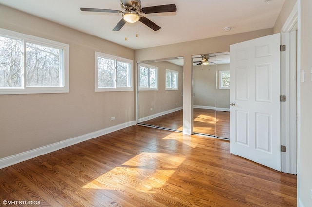 unfurnished bedroom with multiple closets, wood finished floors, a ceiling fan, and baseboards