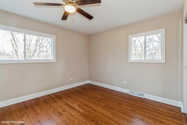 empty room featuring dark wood-type flooring, visible vents, plenty of natural light, and baseboards