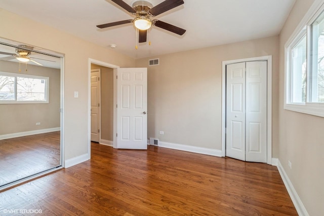 unfurnished bedroom featuring multiple windows, wood finished floors, visible vents, and baseboards