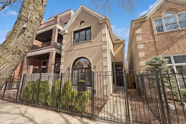 view of front of property with a fenced front yard, brick siding, a balcony, and a gate