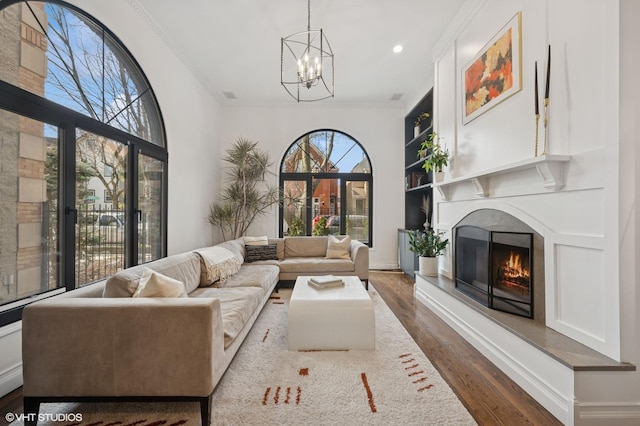 living room featuring a warm lit fireplace, recessed lighting, an inviting chandelier, crown molding, and dark wood-style flooring