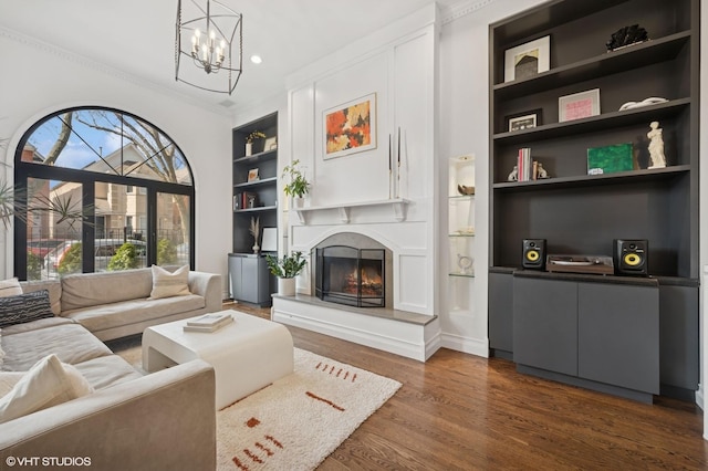 living area with a chandelier, built in features, ornamental molding, a fireplace, and dark wood-style floors