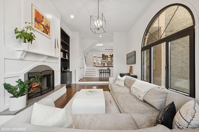 living room with a notable chandelier, wood finished floors, a lit fireplace, and ornamental molding