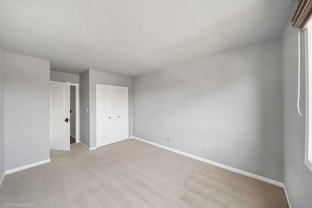 unfurnished bedroom featuring a closet, baseboards, and light colored carpet