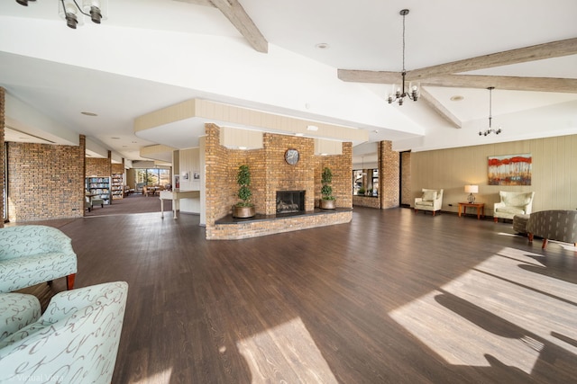 living room with a notable chandelier, lofted ceiling with beams, wood finished floors, brick wall, and a fireplace