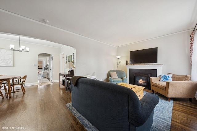 living room with ornamental molding, arched walkways, dark wood-style flooring, and a glass covered fireplace