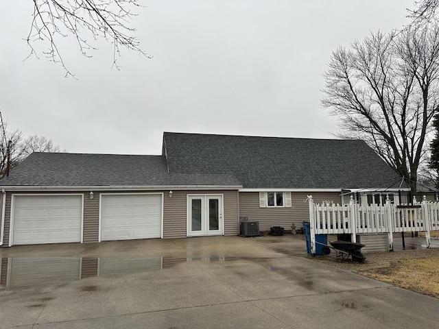 view of front of home with central AC, roof with shingles, a wooden deck, and driveway