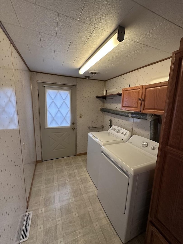 laundry area with visible vents, washer and dryer, cabinet space, light floors, and wallpapered walls