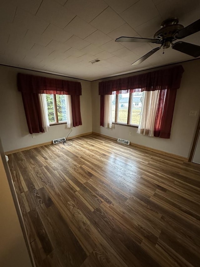 spare room with a ceiling fan, visible vents, baseboards, and wood finished floors