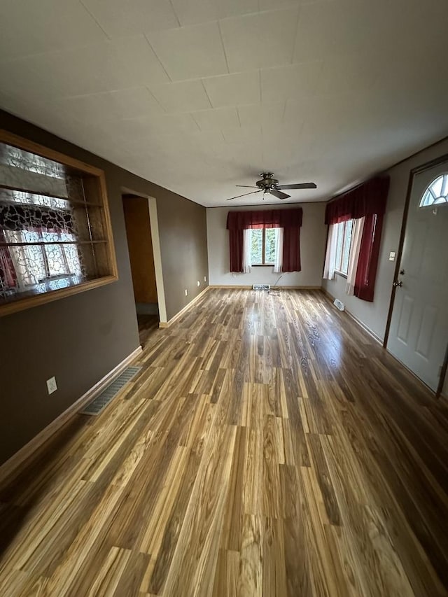 unfurnished living room featuring a ceiling fan, wood finished floors, visible vents, and baseboards