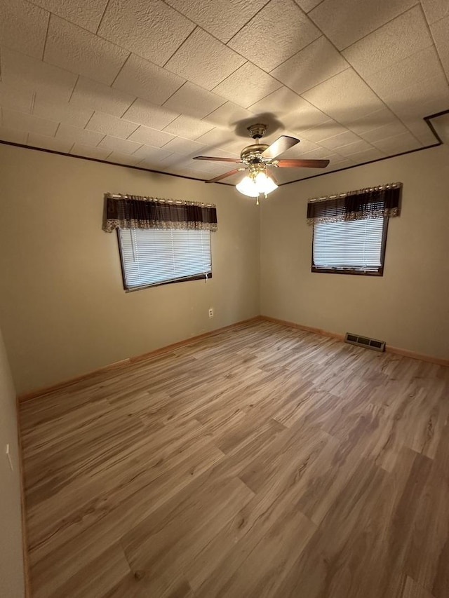 empty room featuring a ceiling fan, baseboards, visible vents, and wood finished floors