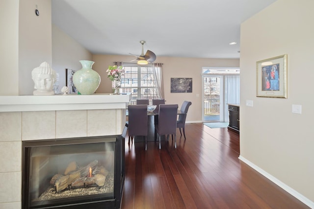 dining room featuring a tiled fireplace, dark wood-type flooring, plenty of natural light, and baseboards