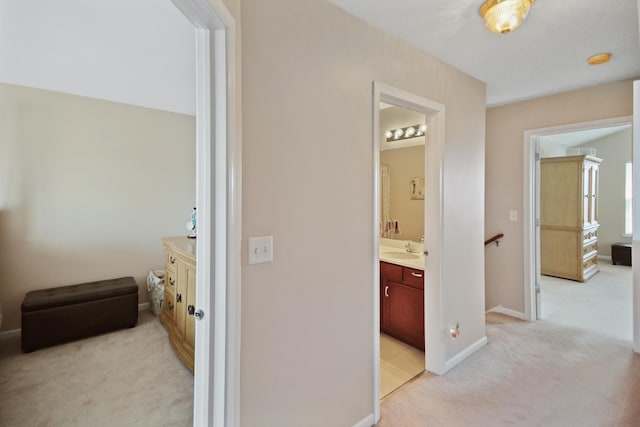 hall featuring light carpet, baseboards, a sink, and an upstairs landing