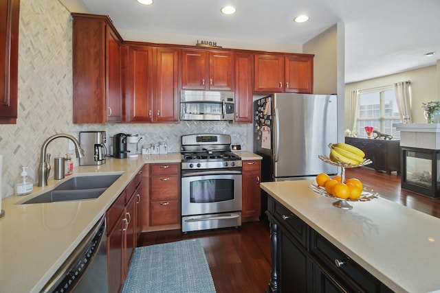 kitchen with appliances with stainless steel finishes, dark wood-type flooring, light countertops, dark brown cabinets, and a sink