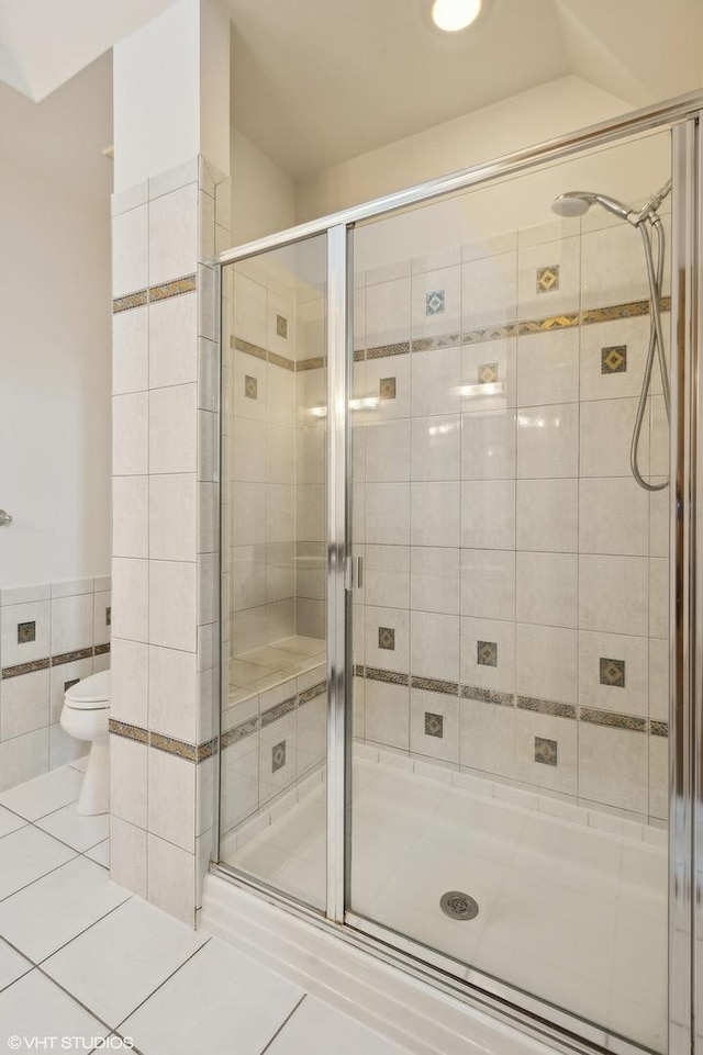 bathroom with tile patterned floors, toilet, tile walls, and a stall shower