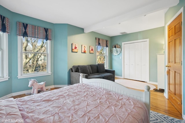 bedroom with baseboards, multiple windows, beam ceiling, and wood finished floors