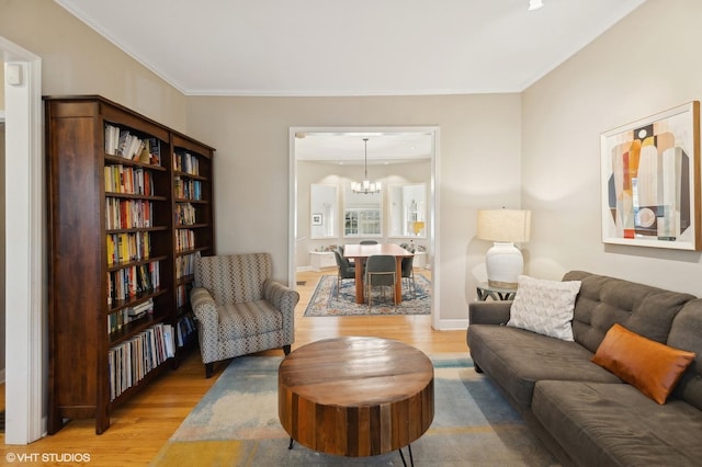 living area featuring a chandelier, light wood-type flooring, baseboards, and ornamental molding