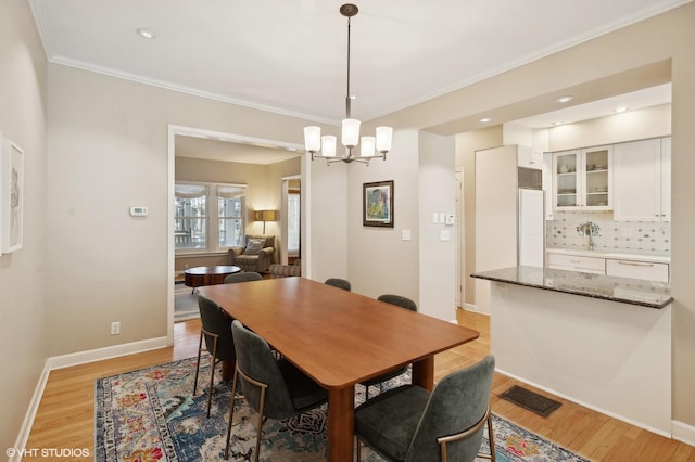 dining area featuring visible vents, baseboards, light wood-style flooring, and crown molding