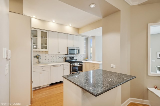 kitchen with a sink, white cabinetry, appliances with stainless steel finishes, a peninsula, and decorative backsplash