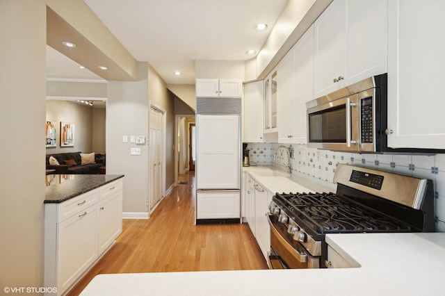 kitchen featuring decorative backsplash, light wood-style floors, white cabinets, stainless steel appliances, and a sink