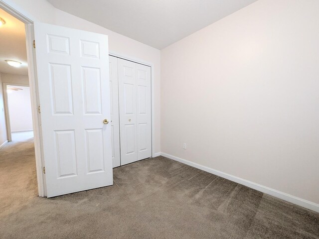 unfurnished bedroom featuring vaulted ceiling, a closet, carpet flooring, and baseboards