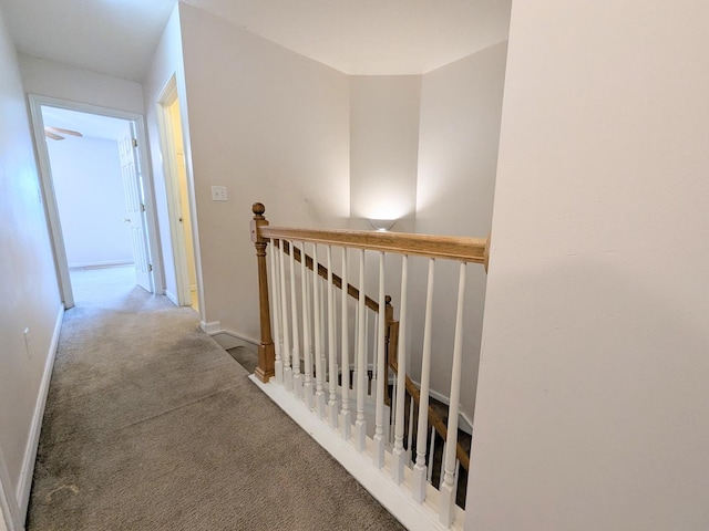 hall featuring carpet, baseboards, and an upstairs landing