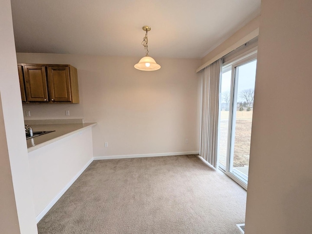 unfurnished dining area featuring light carpet, baseboards, and a sink