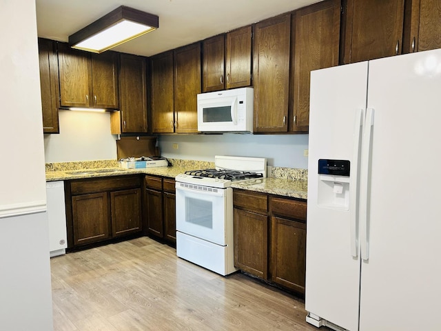 kitchen featuring light wood-style flooring, a sink, dark brown cabinets, light stone countertops, and white appliances