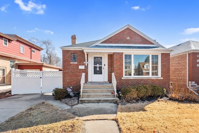 bungalow-style home with brick siding, a chimney, fence, and a gate