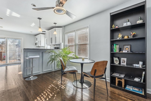 dining space featuring built in shelves, a ceiling fan, baseboards, and dark wood-style flooring