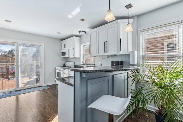 kitchen featuring dark wood-type flooring, decorative light fixtures, dark stone counters, white cabinets, and white appliances